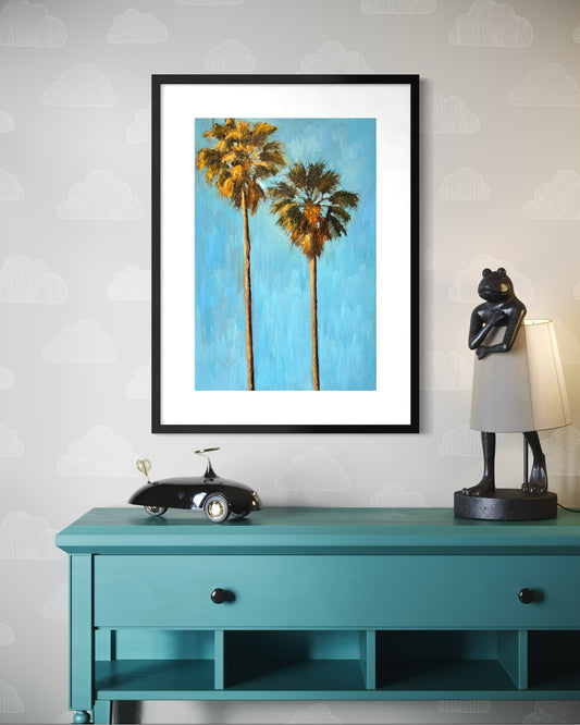 Framed artwork of palm trees on a wall above a teal console table with decorative items.