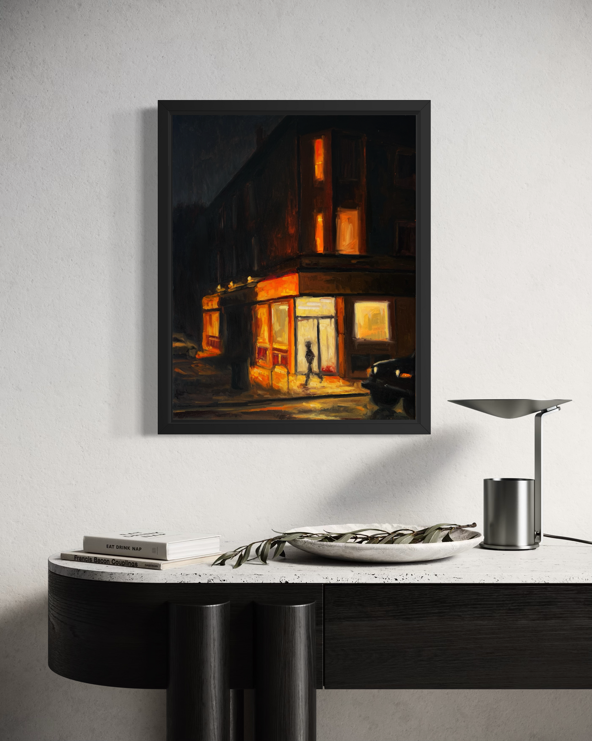 "Corner Store" original oil painting by John Wellington — framed above a sculptural black console with a desk lamp