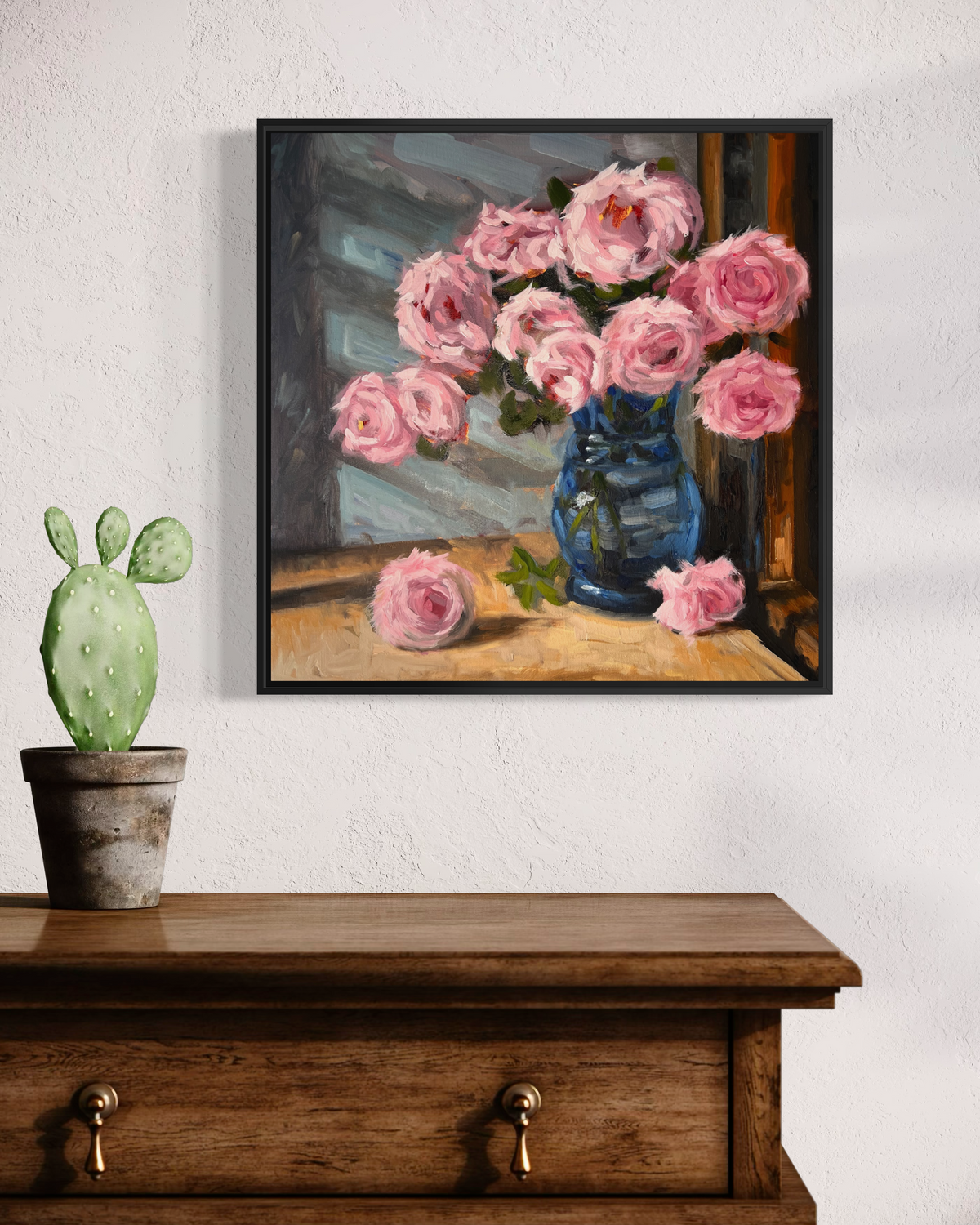 "Pink Roses" original oil painting by John Wellington — black floater frame above a rustic wooden chest