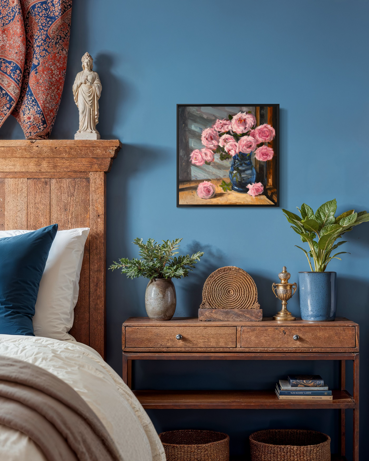 "Pink Roses" original oil painting by John Wellington — framed on a blue bedroom wall above a wooden nightstand